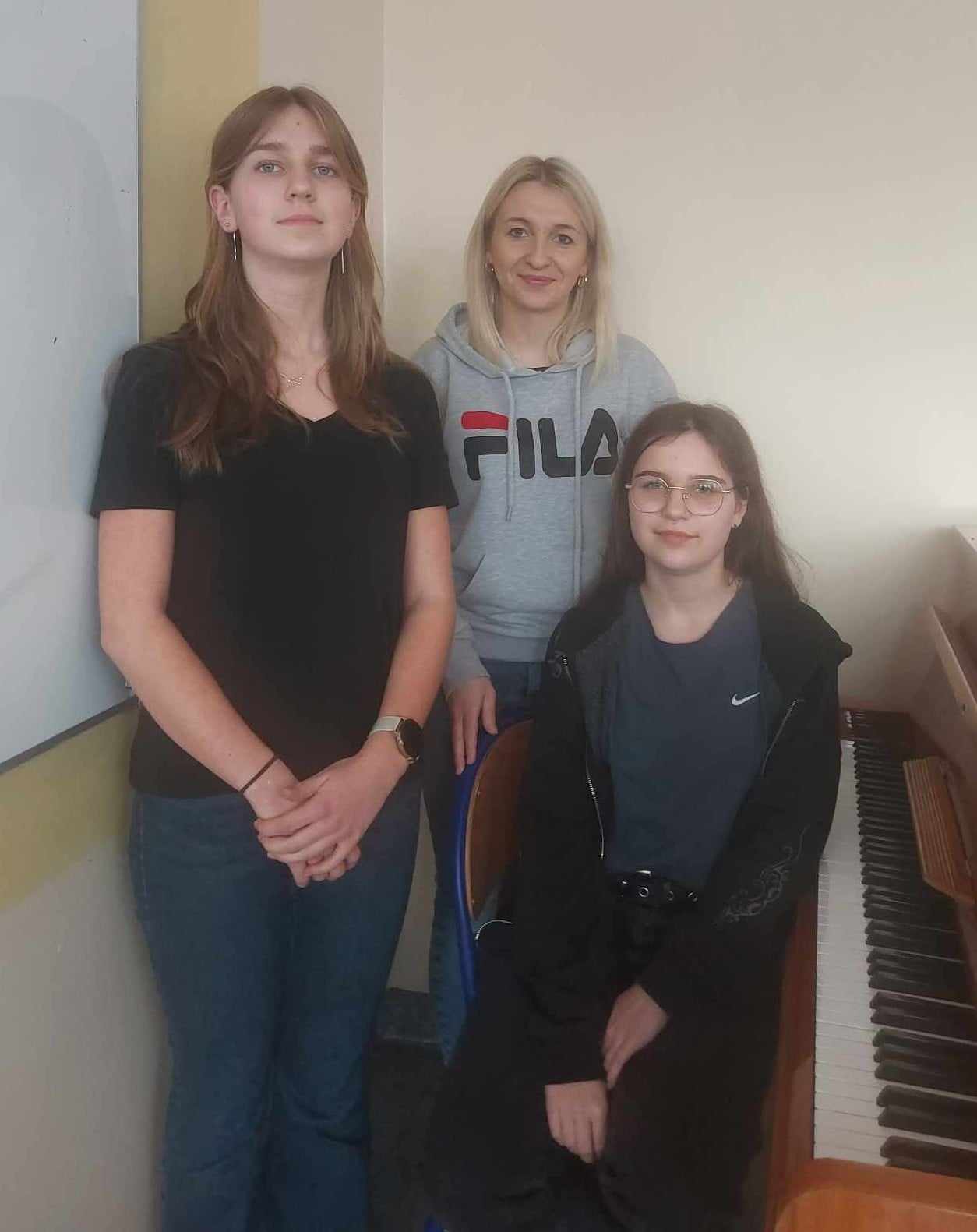 Dwie uczennice i nauczycielka, po prawej klawiatura pianina.